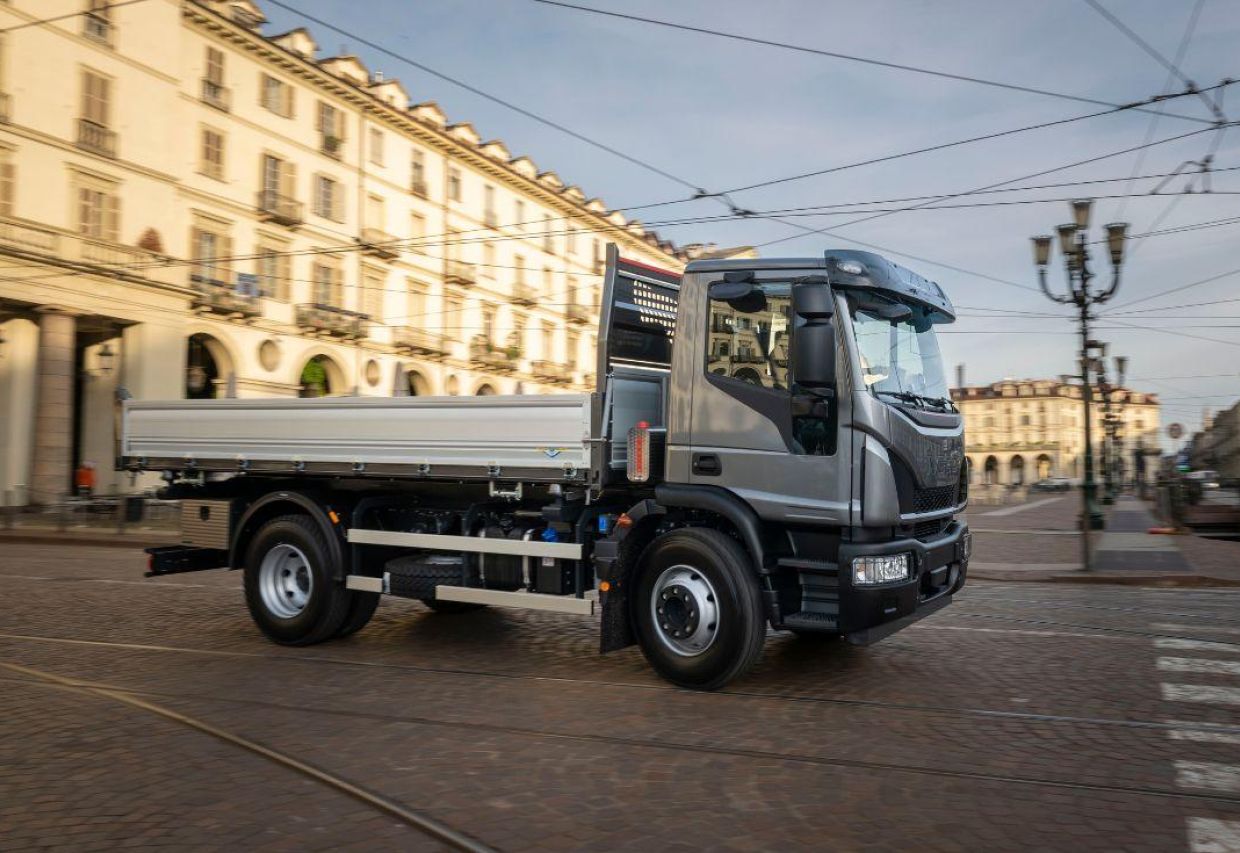 Iveco Eurocargo z szarą kabiną i białą przestrzenią ładunkową jadący miejską ulicą